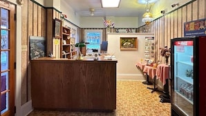 A reception area with a wooden desk, a computer, a refrigerator, and a wall with framed pictures and a Coca-Cola sign. - Stiles Motel Hill View Woodstock NB (Woodstock)