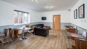 A modern dining area with wooden tables and chairs, a black leather couch, and a television on the wall. - Flexistay Aparthotel Sutton (Sutton)