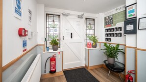 A hotel lobby with a reception desk, two doors, potted plants, a fire extinguisher, and informational posters on the walls. - Flexistay Aparthotel Sutton (Sutton)