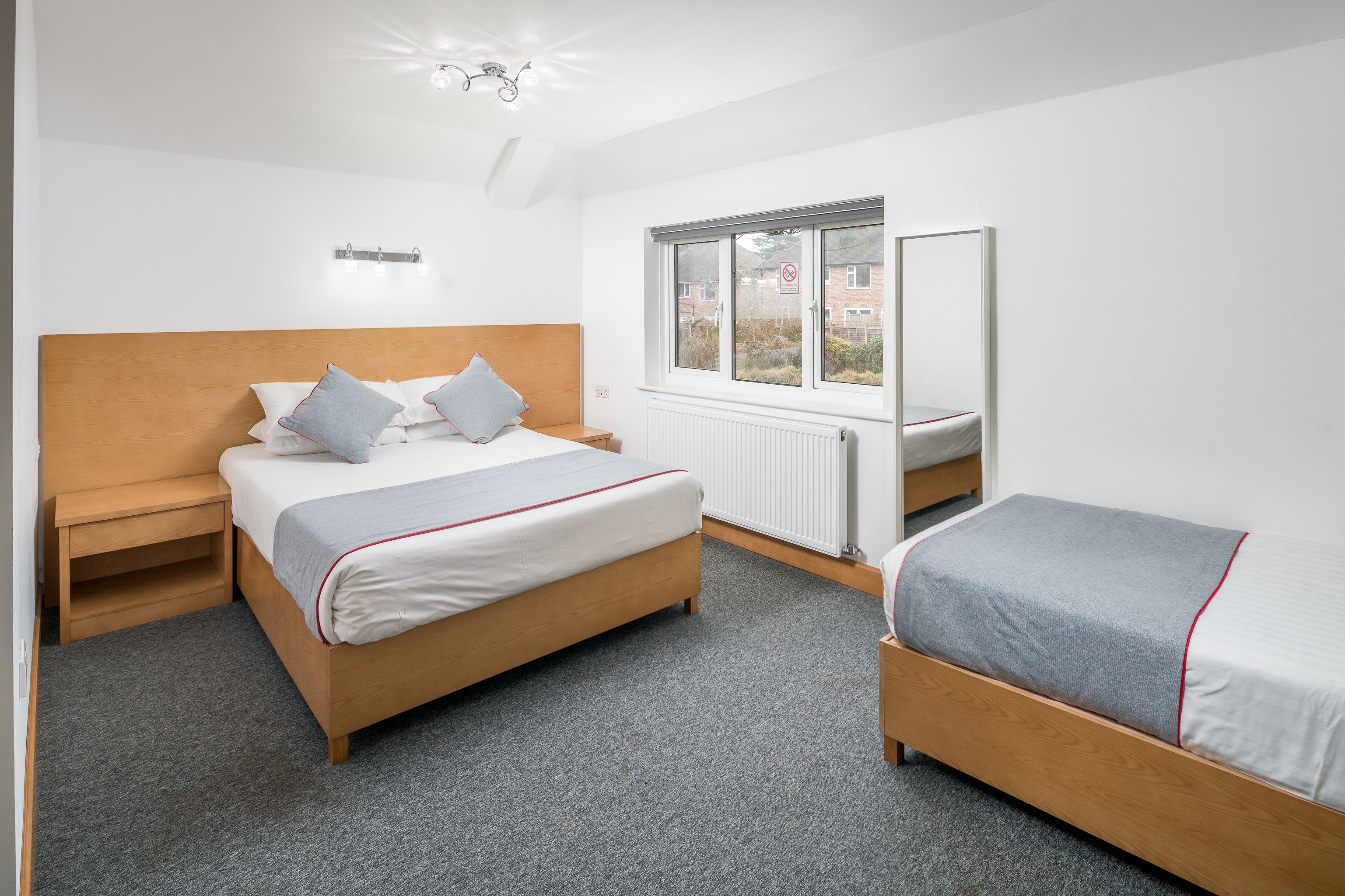 A bedroom with a large bed, a smaller bed, a nightstand, a window, and a radiator.