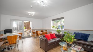 A modern living room with a brown leather sofa, red cushions, a glass coffee table, and a dining area with wooden chairs and a table. - Flexistay Aparthotel Sutton (Sutton)
