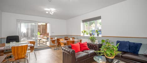 Una sala de estar moderna con un sofá de cuero marrón, cojines rojos, una mesa de centro de vidrio y una zona de comedor con sillas y una mesa de madera.