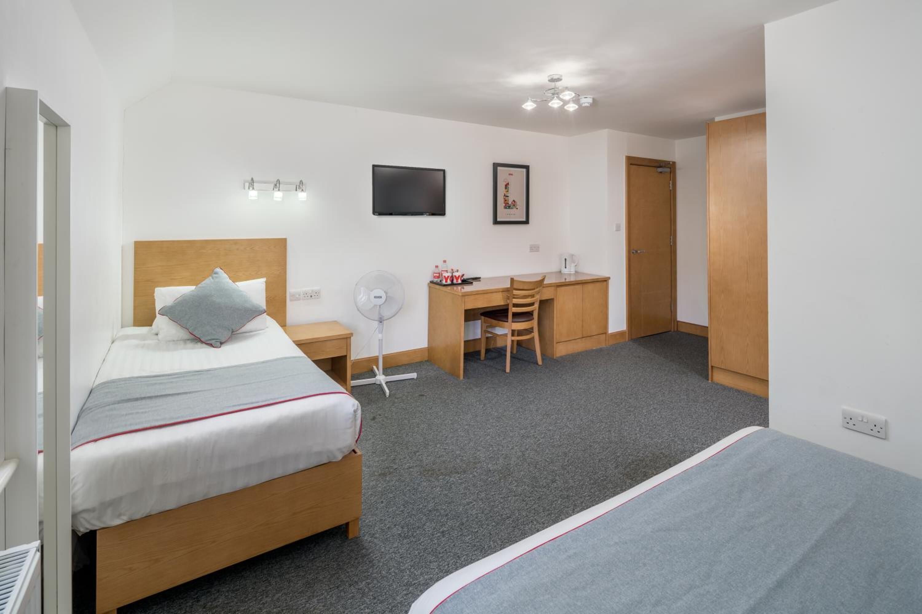 A hotel room with a bed, a desk, a chair, a TV, and a door.