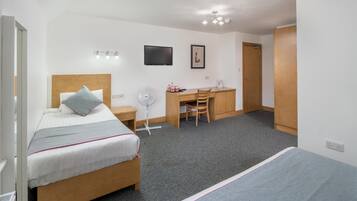 A hotel room with a bed, a desk, a chair, a TV, and a door.