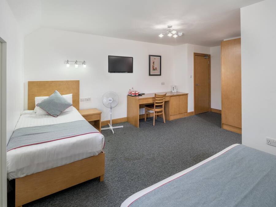 A hotel room with a bed, a desk, a chair, a TV, and a door.