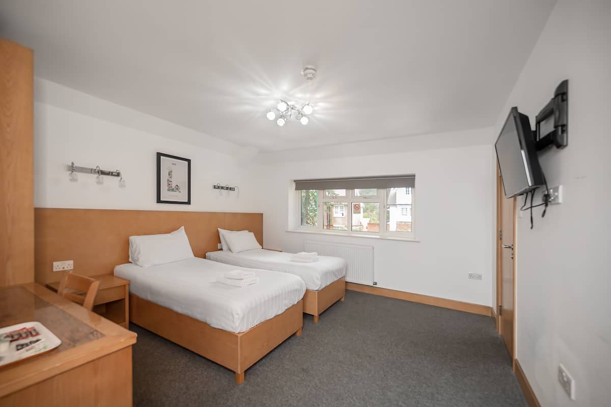 A hotel room with two single beds, a desk with a chair, a television mounted on the wall, and a window providing a view of the outside.