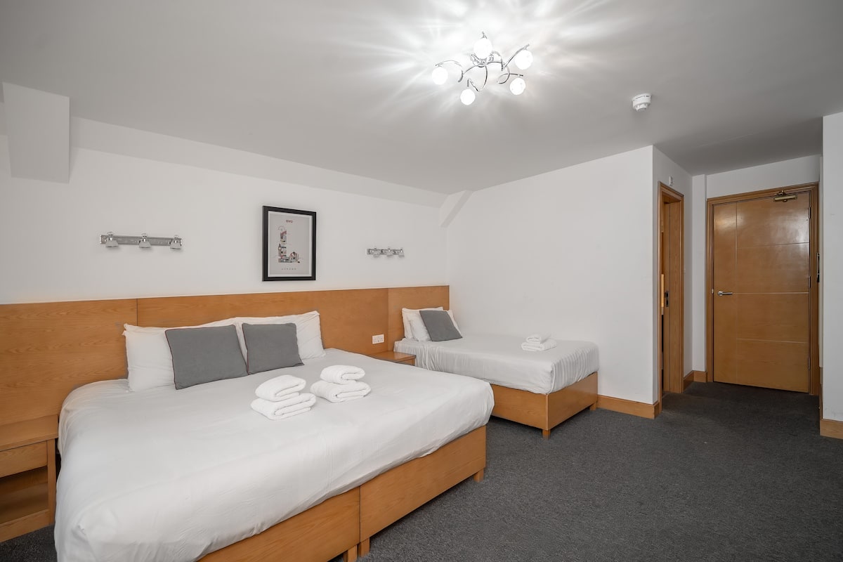 A hotel room with two beds, a wooden headboard, a chandelier, a framed picture on the wall, and a door.