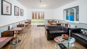 A modern dining area with wooden tables and chairs, a leather sofa, and a glass coffee table. - Flexistay Aparthotel Sutton (Sutton)
