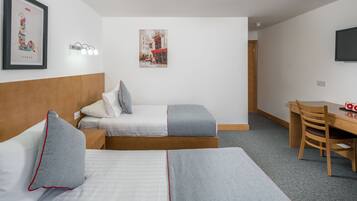 Ett hotellrum med två sängar, ett skrivbord, en stol och en tv på väggen.