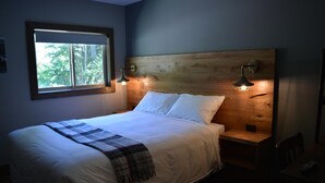 Ein ordentlich bezogenes Bett mit einer Karo-Decke, einem Holzkopfteil und zwei Nachttischlampen.