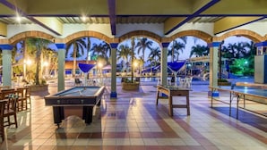 Ein Poolbereich mit Pooltisch, Liegestühlen und einer überdachten Sitzecke mit Blick auf Palmen.