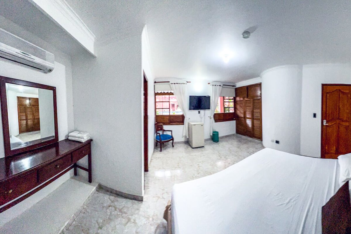 Une chambre d’hôtel comprenant un lit, un bureau avec un miroir, une petite chaise, une télévision et une armoire.