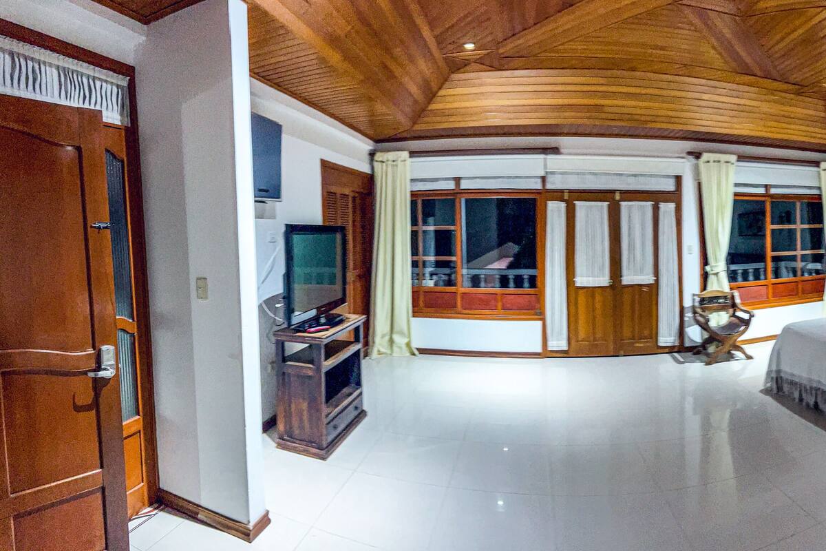 Une chambre spacieuse avec un grand lit, un plafond en bois et un téléviseur placé dans un coin.