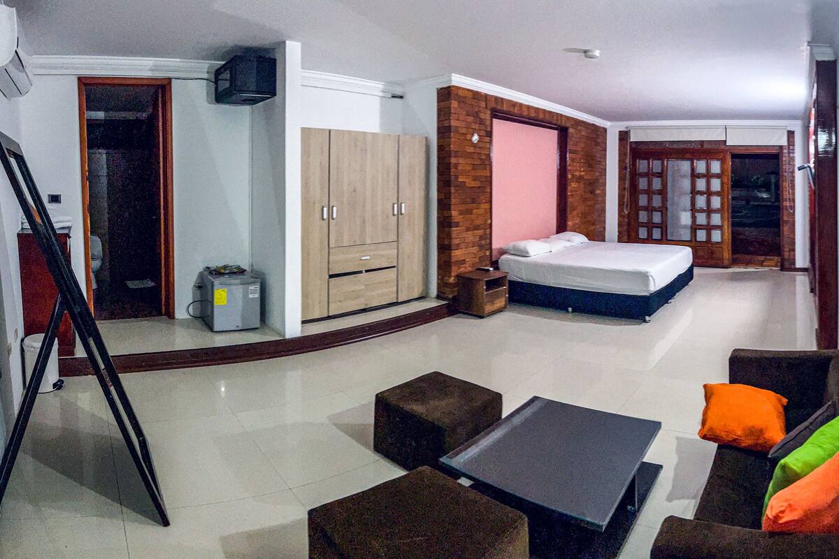 Une chambre d’hôtel avec un lit, une petite table, un canapé avec des coussins, un miroir et une armoire.