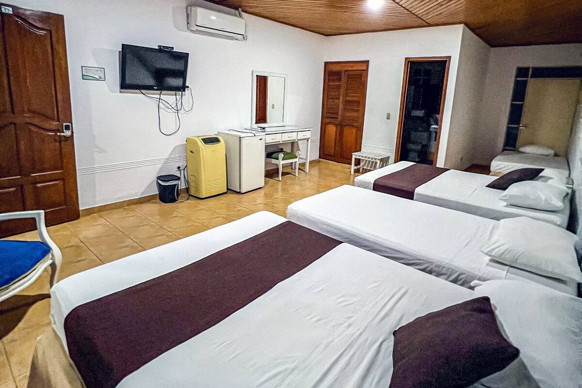 Une chambre d’hôtel avec quatre lits, un bureau, une chaise, une télévision et un appareil de climatisation.