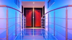 Een moderne hotelgang met glazen balustrades, een spiegelende vloer en een plafond met blauwe verlichting.