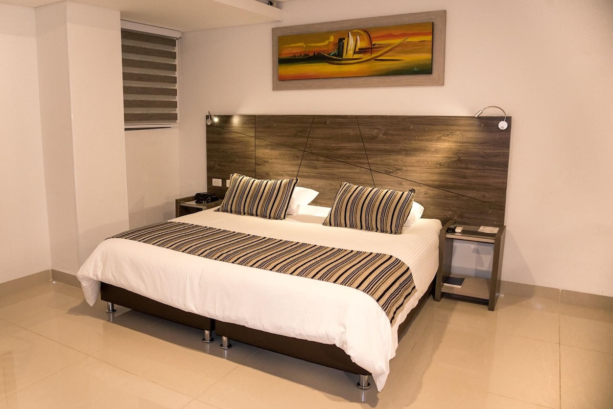 A modern bedroom with a large bed, striped bedding, a wooden headboard, a nightstand, and a painting on the wall.