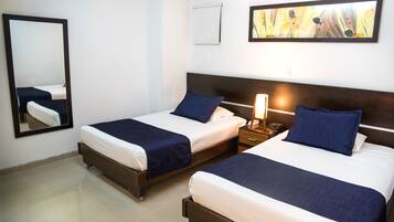 Una habitación de hotel con dos camas, una mesita de noche con lámpara, un espejo y un cuadro en la pared.