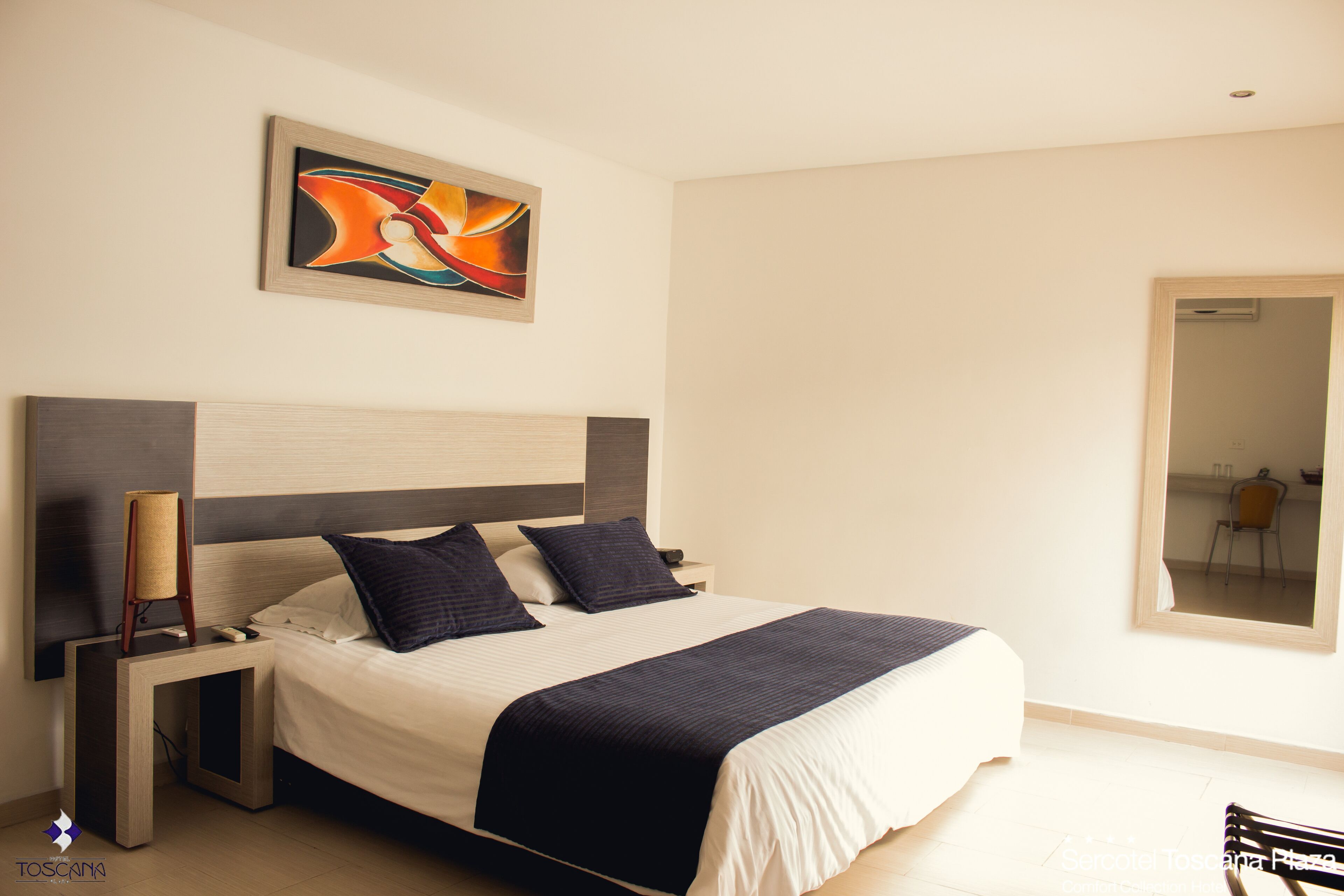A modern hotel room with a large bed, a nightstand, a lamp, and a painting on the wall.