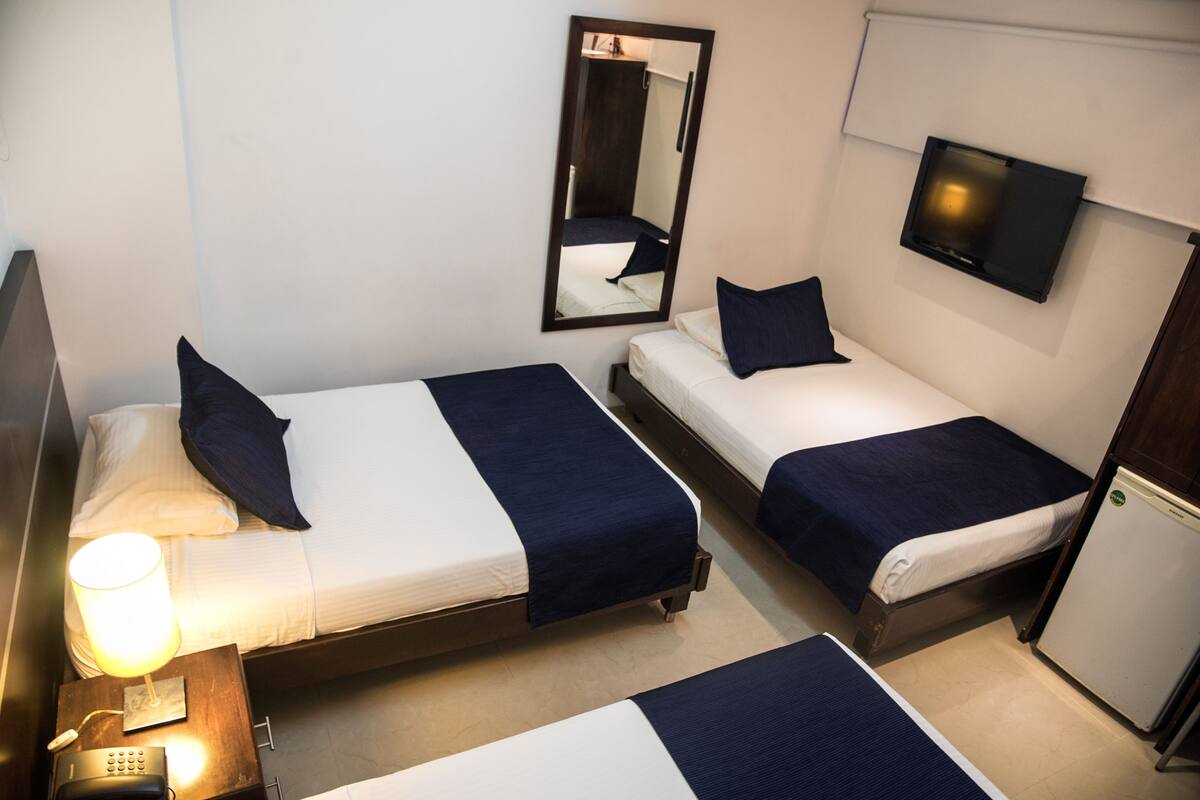 A hotel room with two beds, a nightstand with a lamp, a mirror, a television, and a refrigerator.