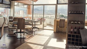 Een moderne hotel lobby met uitzicht over de stad, een wijnrek en een eetgedeelte met tafels en stoelen.