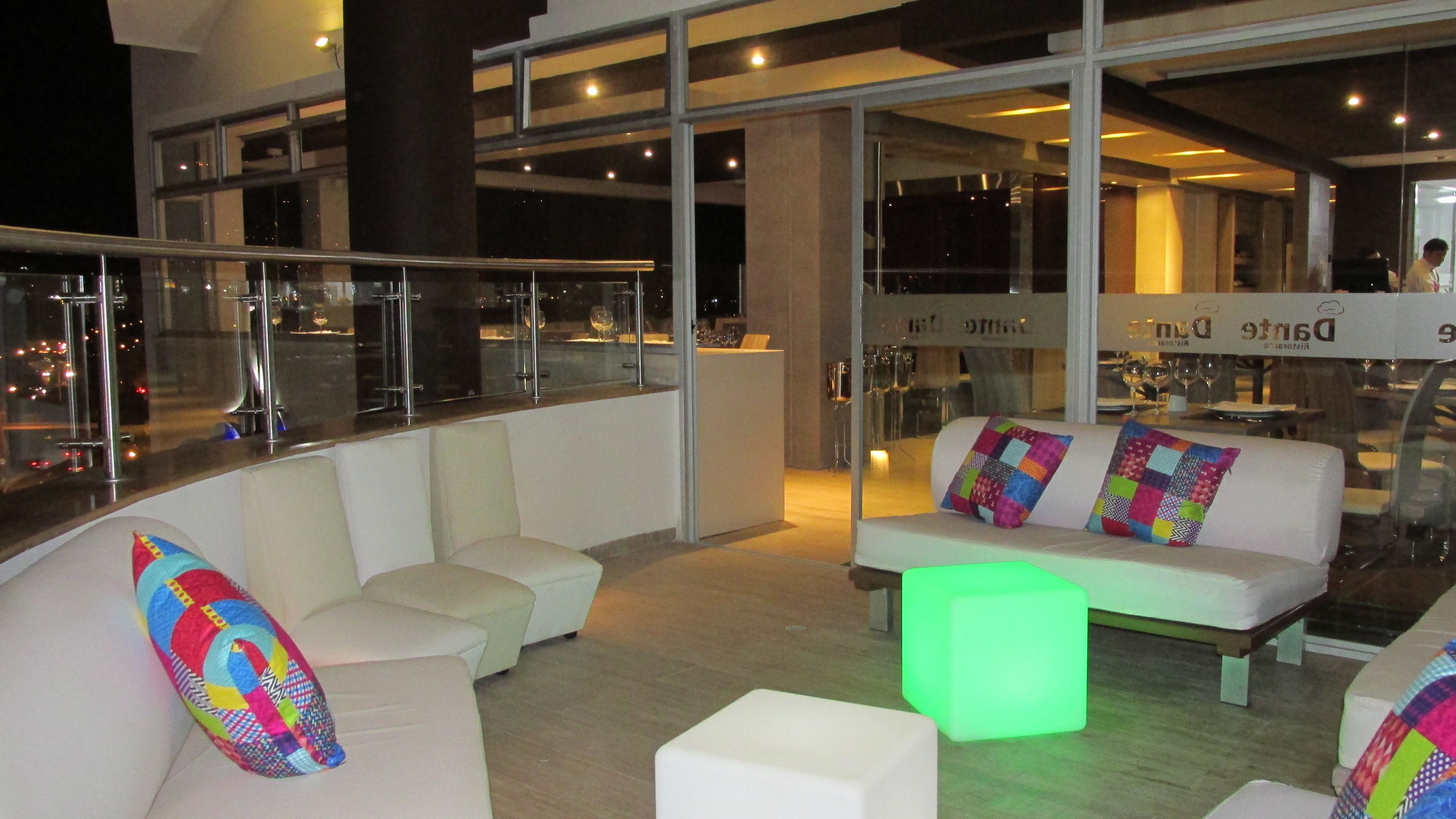 A modern lounge area with a curved white sofa set, colorful cushions, and a glowing green cube.