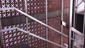 Una escalera con barandillas de metal y un muro ajedreado al fondo.