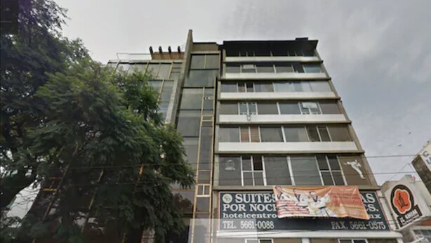 Un hotel de varios pisos con un letrero que anuncia 'SUITES POR NOCHE' e información de contacto.