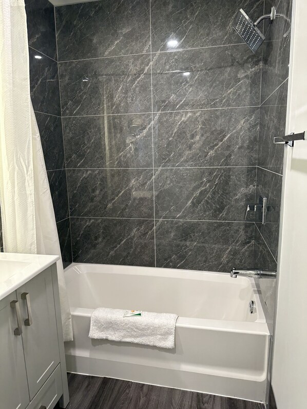 A bathroom with a white bathtub, a shower, and dark marble tiles.
