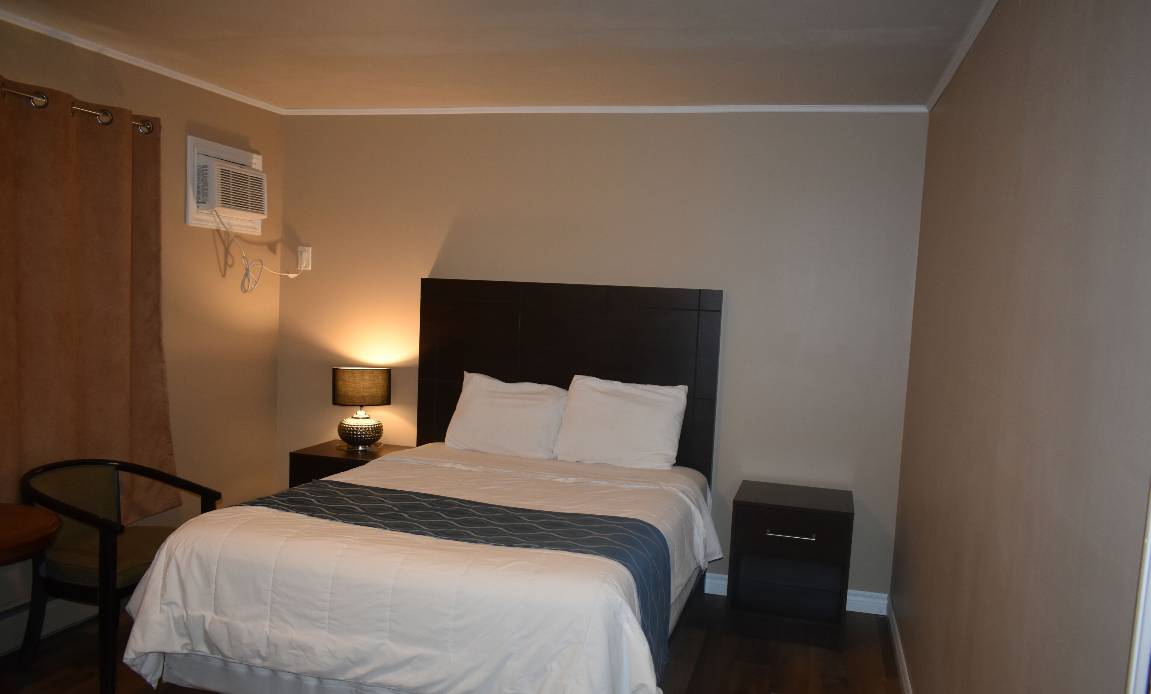 A bedroom with a bed, a nightstand, a chair, and a lamp.