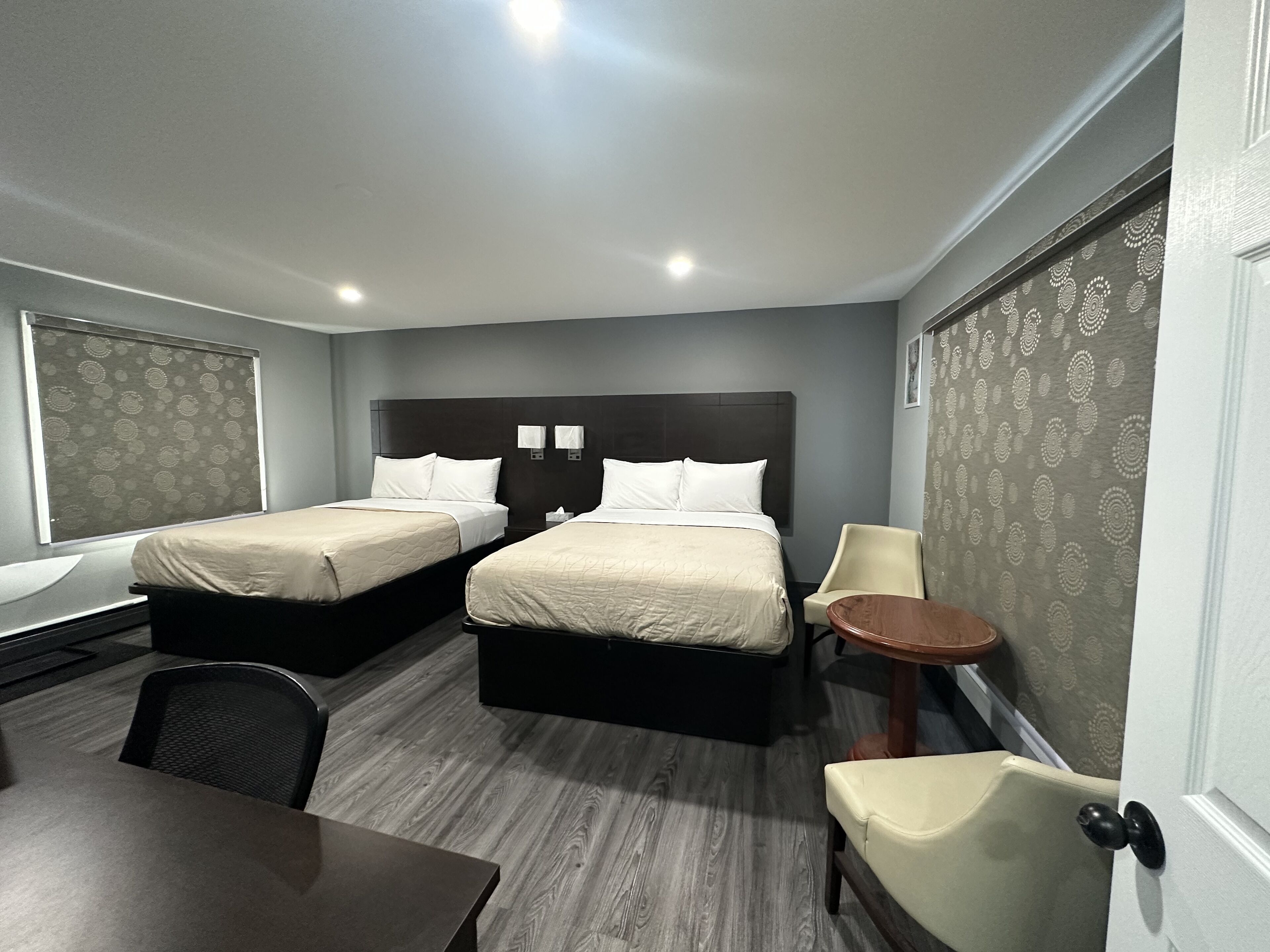 A hotel room with two beds, a desk, a chair, and a small table.