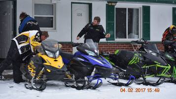 A building with numbered doors, snow-covered ground, and snowmobiles parked in front.