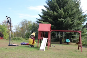 Une aire de jeux avec une balançoire, un toboggan et un petit véhicule.