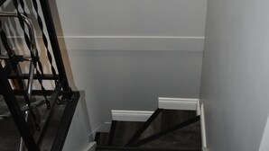 Uma escadaria com degraus de madeira escura e corrimãos de metal preto, que leva a um patamar com rodapé branco.
