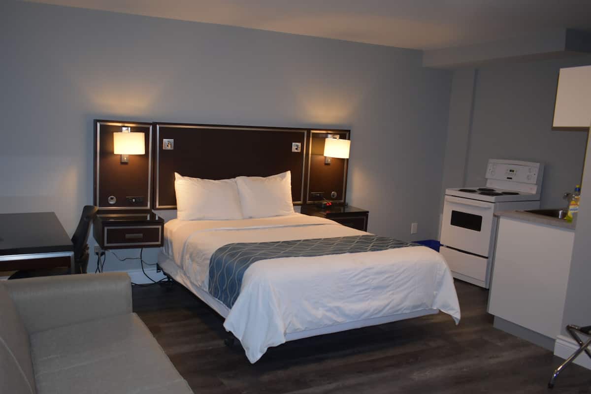 A hotel room with a bed, a desk, a chair, a small kitchenette, and a TV.