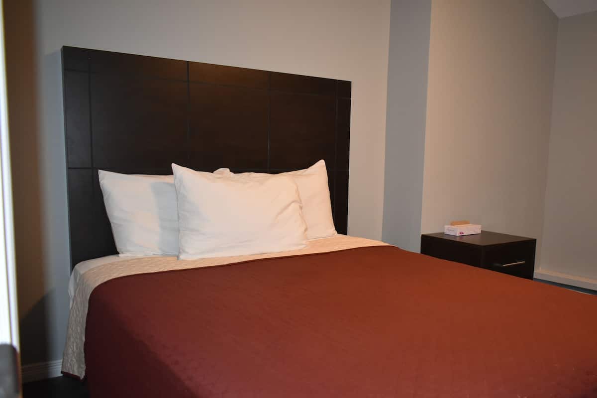 A neatly made bed with white pillows and a brown bedspread in a hotel room.