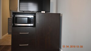 Uma cozinha compacta com micro-ondas embutido, um refrigerador pequeno e uma TV de tela plana instalada acima do micro-ondas.