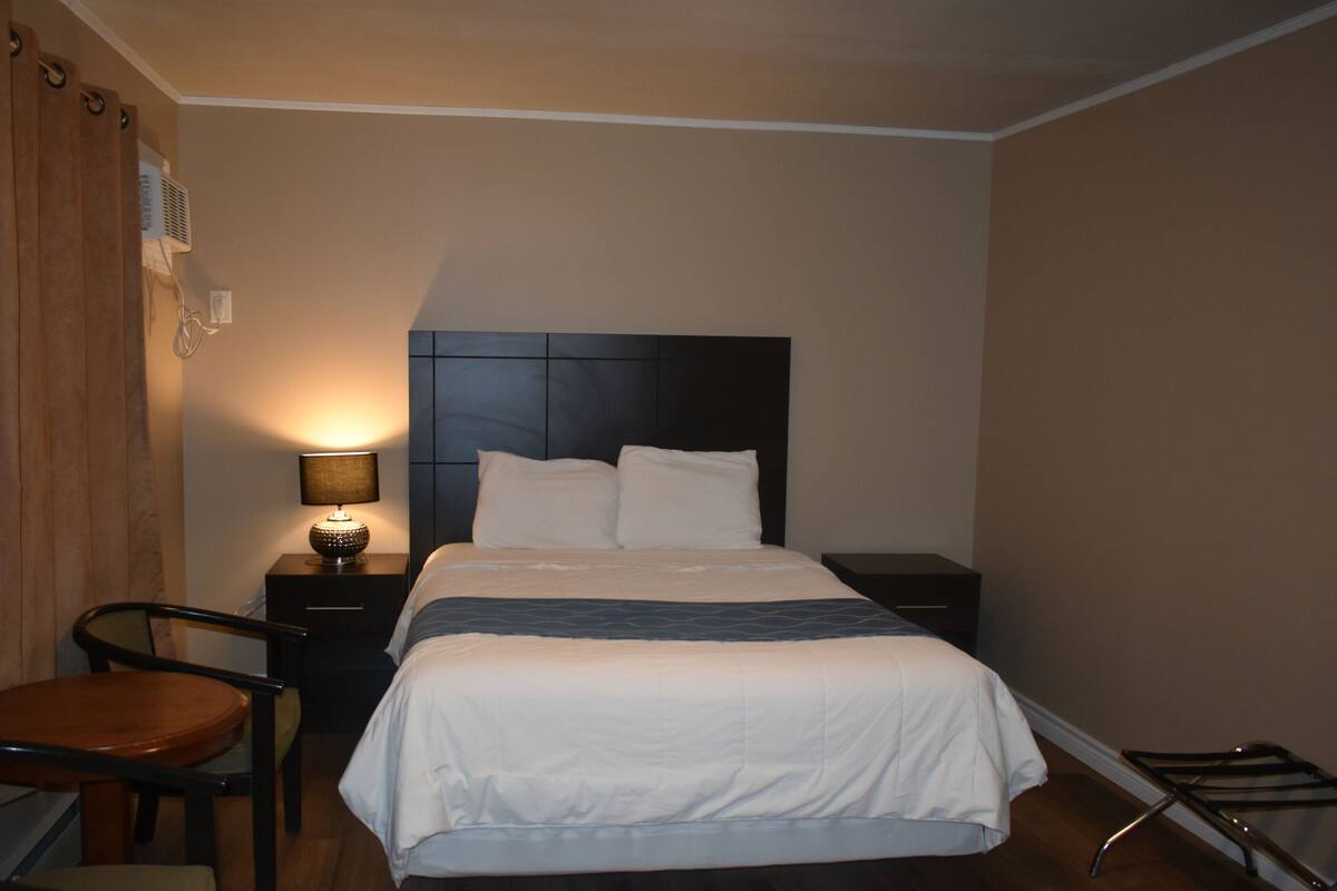 A hotel room with a bed, bedside tables, a lamp, a chair, and a desk.