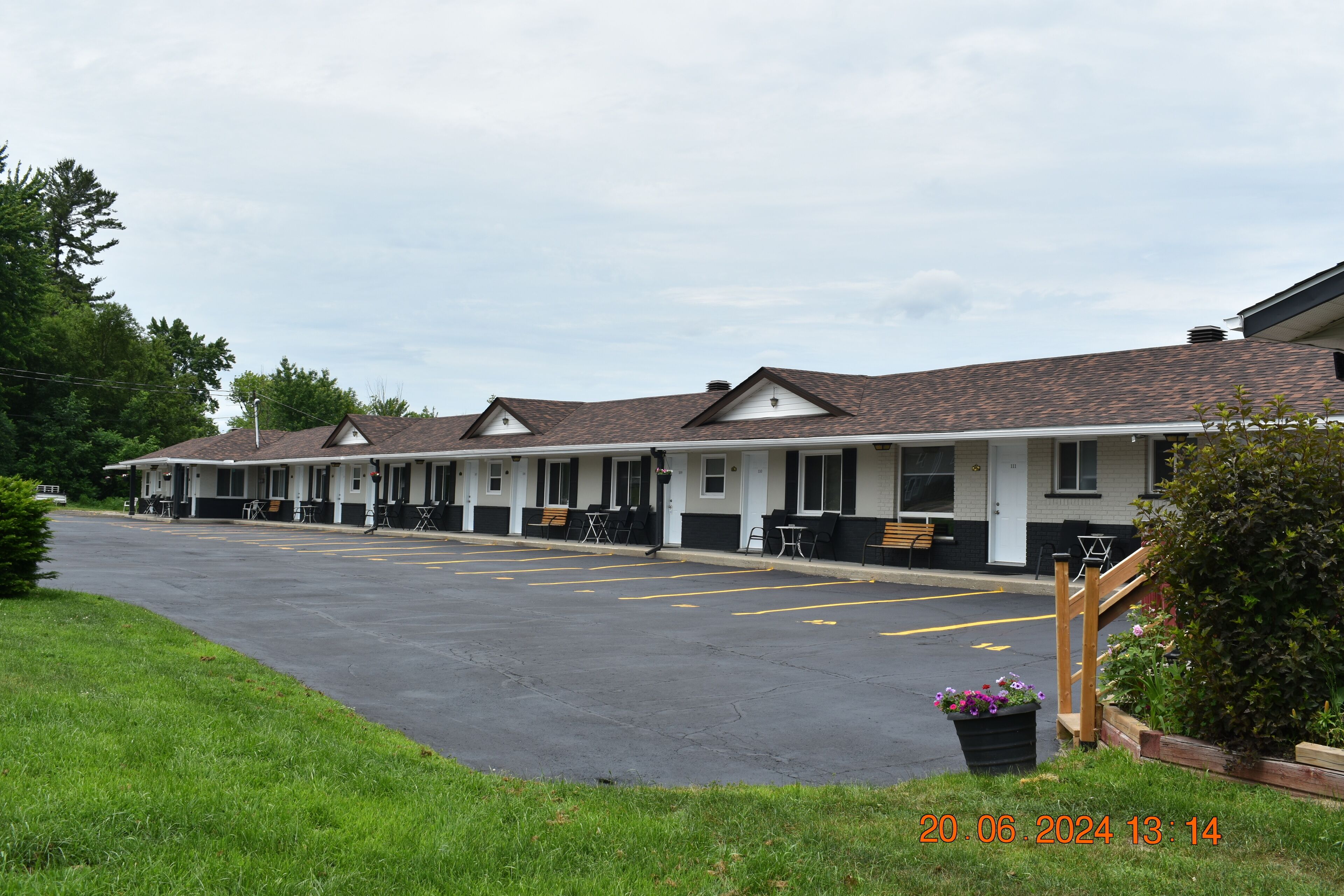 Un motel con una fila de habitaciones, un estacionamiento y un pequeño jardín.