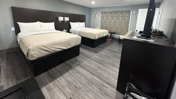 Quarto de hotel com duas camas, uma escrivaninha, uma cadeira e uma televisão.