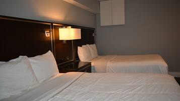 A hotel room with two beds, a nightstand, a lamp, and a wall-mounted cabinet.