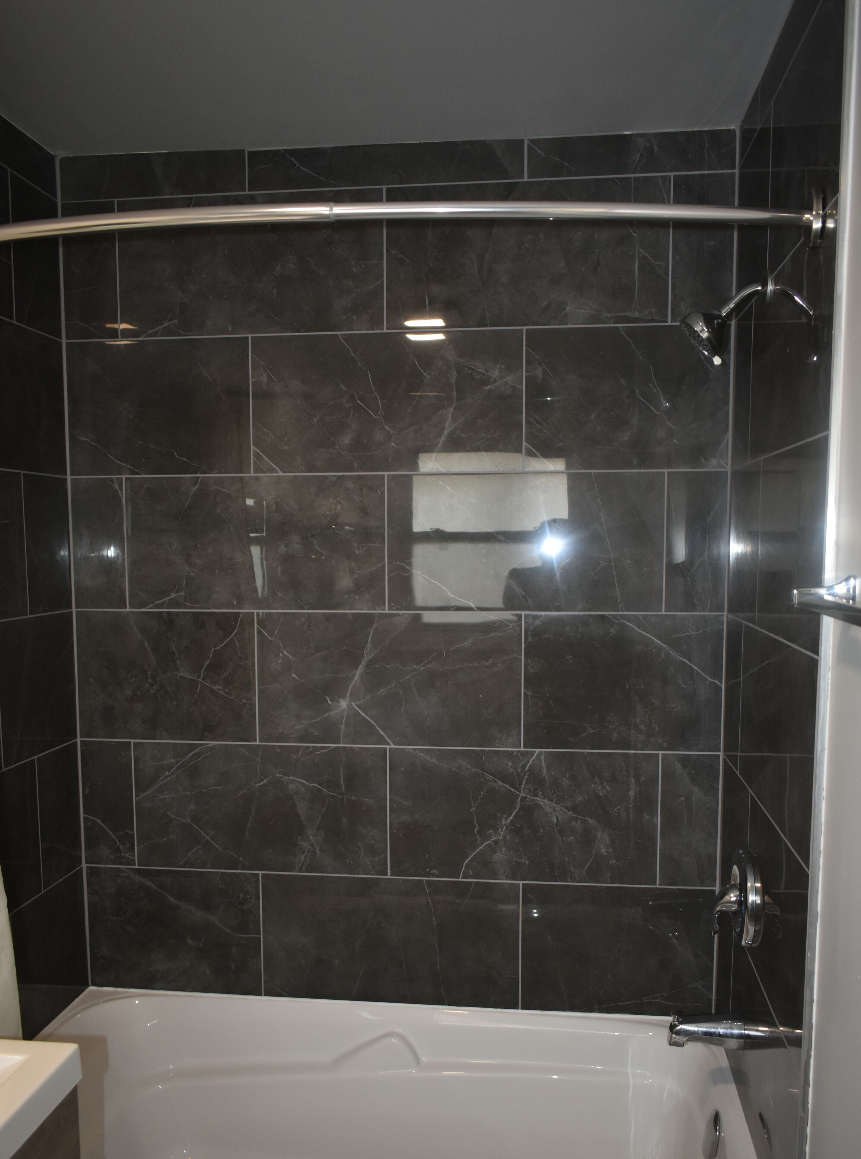 A modern bathroom with dark marble tiles, a bathtub, and a shower area.