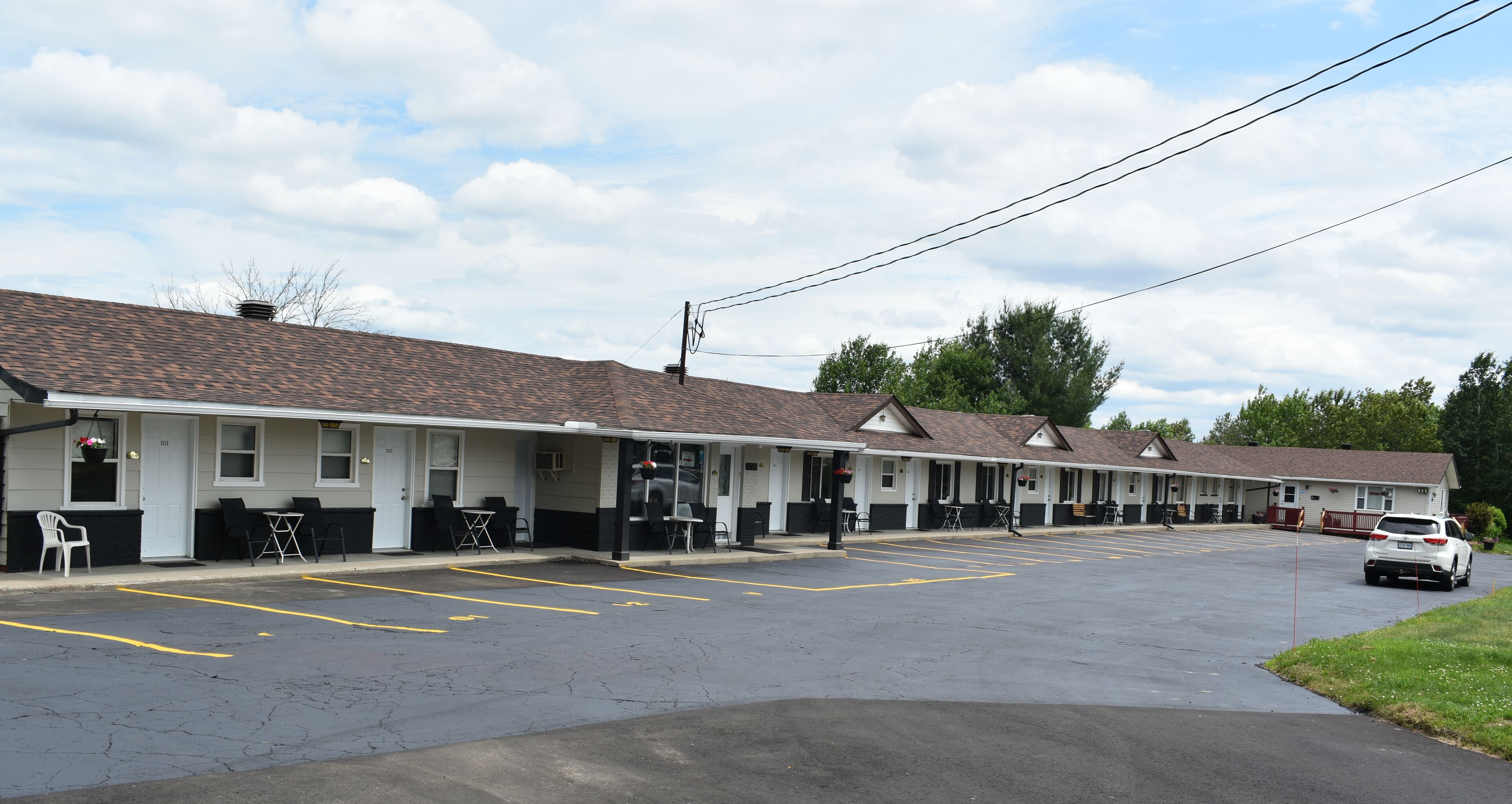A motel with multiple rooms, a parking lot, and a white car parked in the lot.