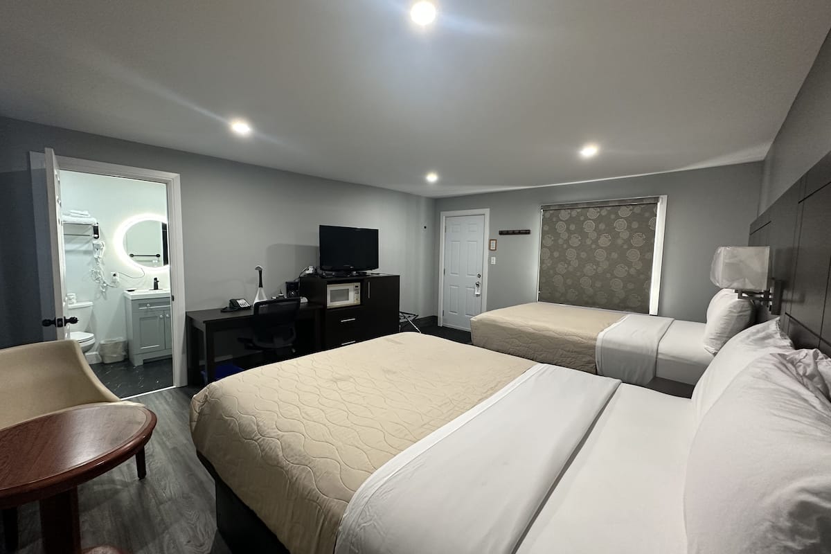 A hotel room with two beds, a desk with a television, a bathroom, and a small table.