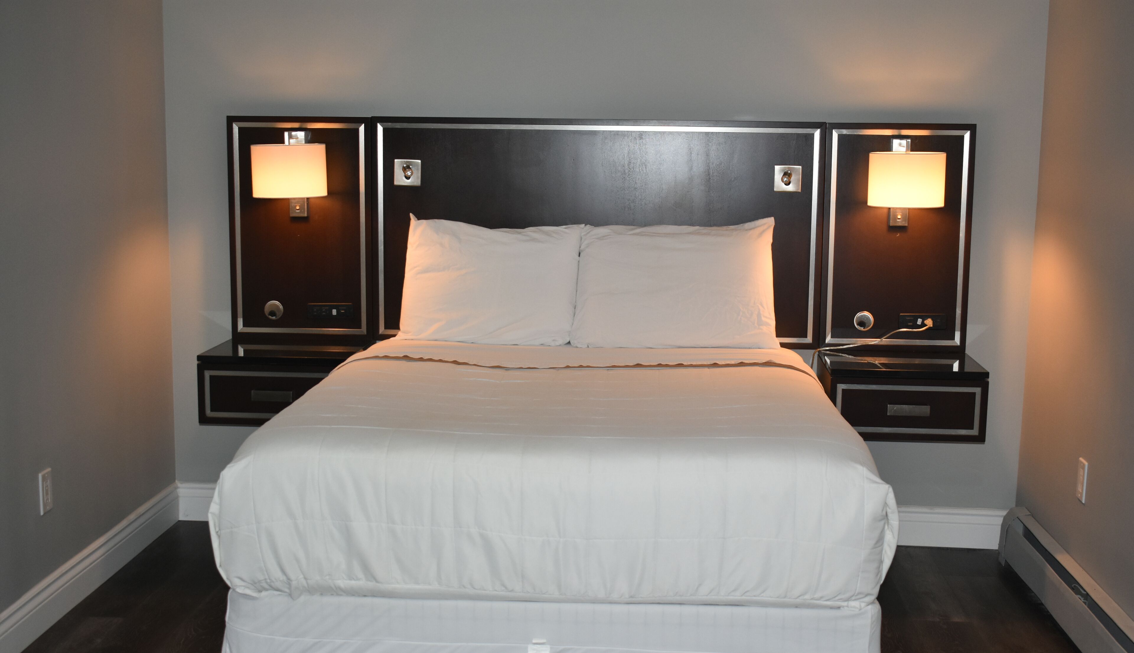 A double bed with a wooden headboard, two bedside tables with lamps, and a neutral-colored wall.