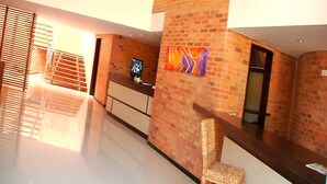 A reception area with a brick wall, a reception desk, a chair, and a large window with blinds. - Hotel Toscana Oriente (El Carmen de Viboral)
