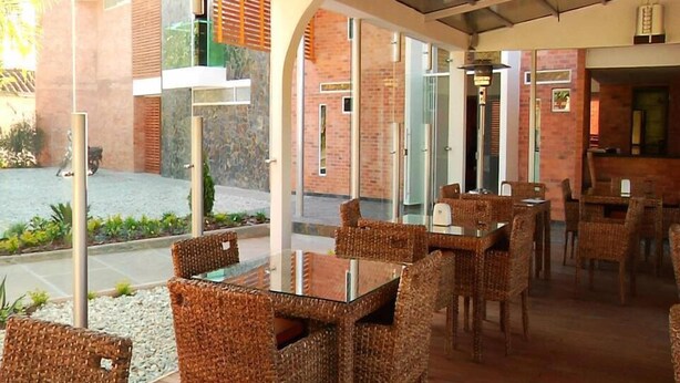 A restaurant with wicker furniture, glass partitions, and a brick exterior. - Hotel Toscana Oriente (El Carmen de Viboral)