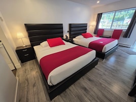 Habitación de hotel con dos camas, una mesita de noche, una lámpara y una ventana con vistas.