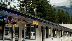 A motel with outdoor seating, a neon sign, and a mountain backdrop. - Alpine Motel (Hope)
