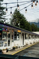 Un motel con asientos exteriores, un letrero de neón y montañas al fondo.